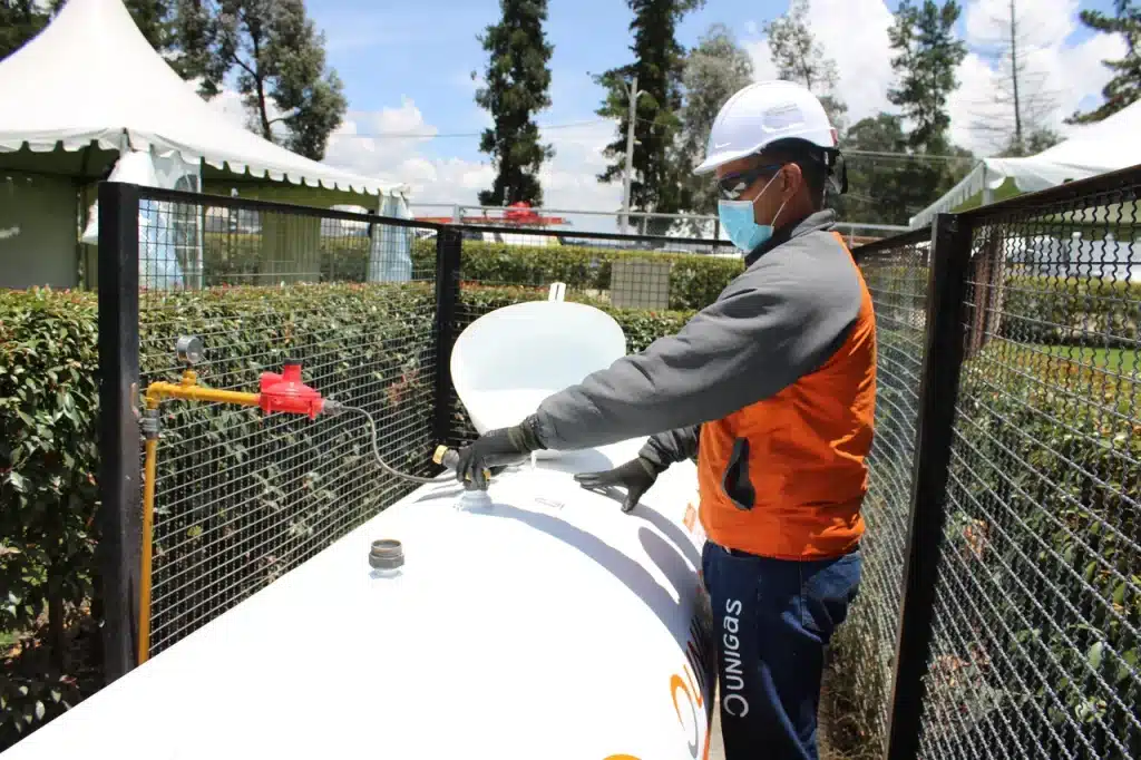 Operario con casco y mascarilla trabajando junto a un tanque de GLP en una zona cercada.